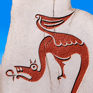 A carved stone featuring a stylized red depiction of a dragon-like creature with wings, shown against a bright blue sky.