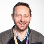 Nic Longo wearing a zip-up sweater and a lanyard, shown against a plain light background.