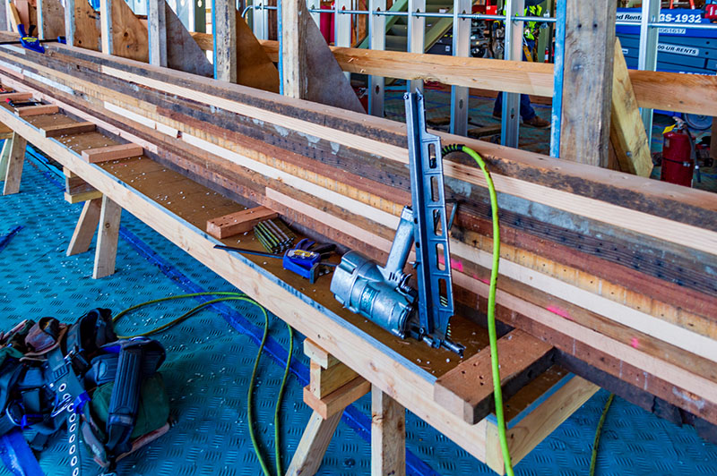 Workbench with stacked wooden boards and construction tools, including a nail gun and fasteners.
