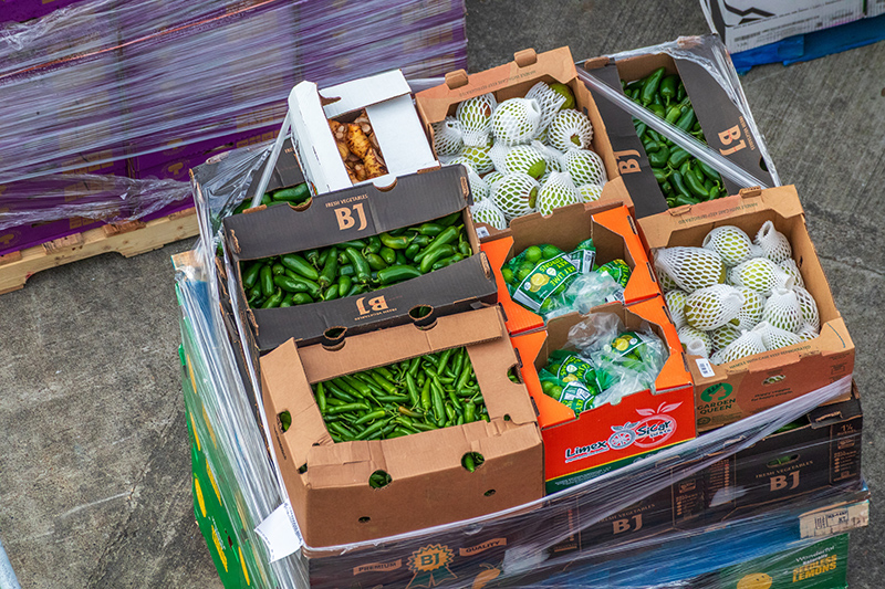 Boxes of assorted produce, including peppers and fruit, stacked on a pallet.