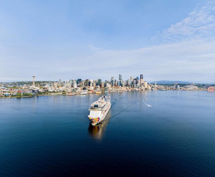 A cruise ship sails across Elliott Bay toward downtown Seattle, with the city skyline and the Space Needle visible in the background.