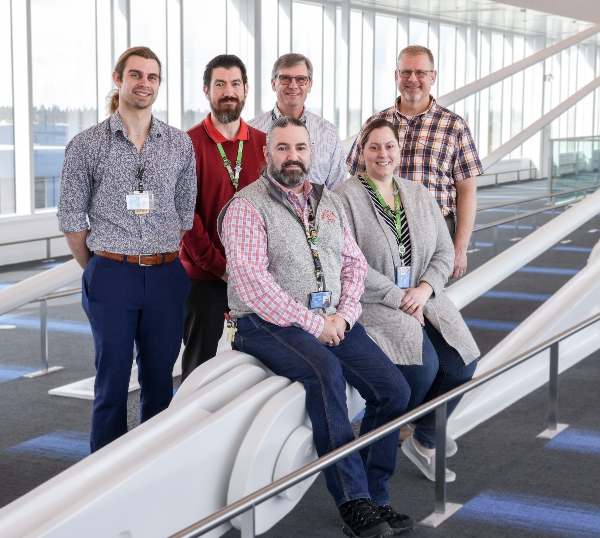 Group photo of six people standing and sitting in a bright, modern airport walkway.