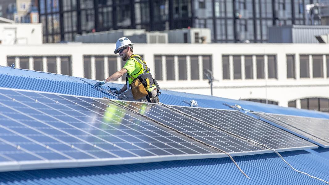 Engineer instals solar panels on the blue metal roof of Pier 69 Port headquarters building.