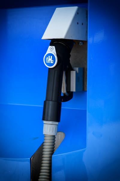 A close-up view of a hydrogen fuel pump nozzle attached to a blue fuel dispenser.