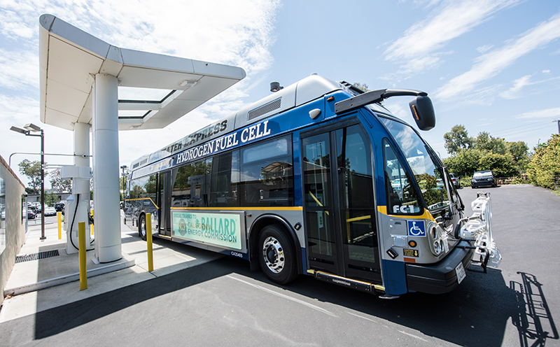 A hydrogen fuel cell bus is parked under a refueling station canopy.