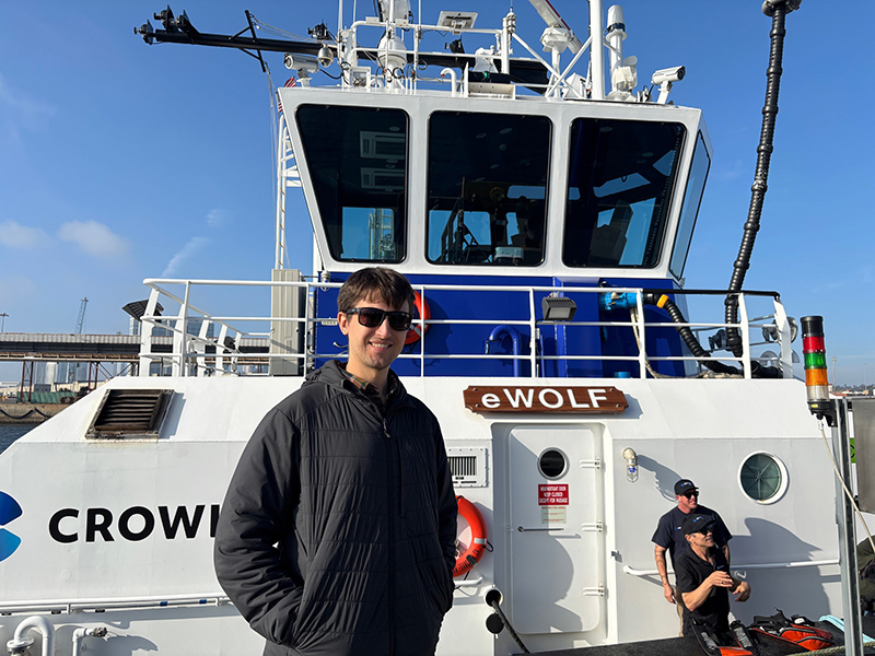 Jack Winterhalter stands on the deck of the eWolf electric tugboat, with the vessel’s wheelhouse behind them.