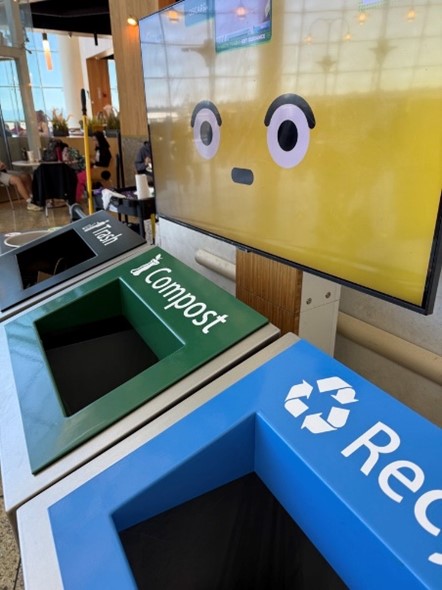 A display screen showing a cartoon face is mounted above three waste-sorting bins labeled Trash, Compost, and Recycle.