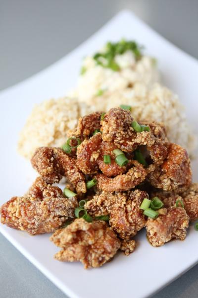 A plate of garlic fried chicken topped with chopped green onions, served with rice and a creamy side dish at Poke to the Max.