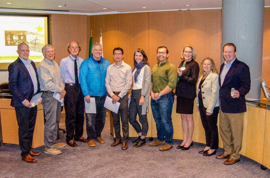 A group of people standing together in a meeting room holding papers and awards, representing the Q4 Innovation Award winning project team with Executive Director Steve Metruck.