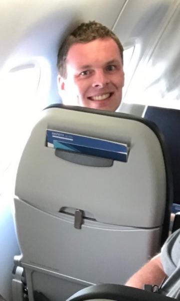 Ryan Fox smiling over the top of an airplane seatback.