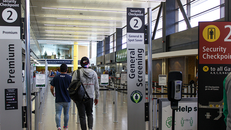 People walk into an airport security area with lanes marked for premium and general screening.