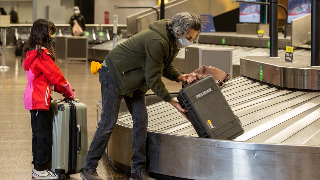 Father and daughter collect baggage from a carousel at sEA Airport in a largely empty terminal.