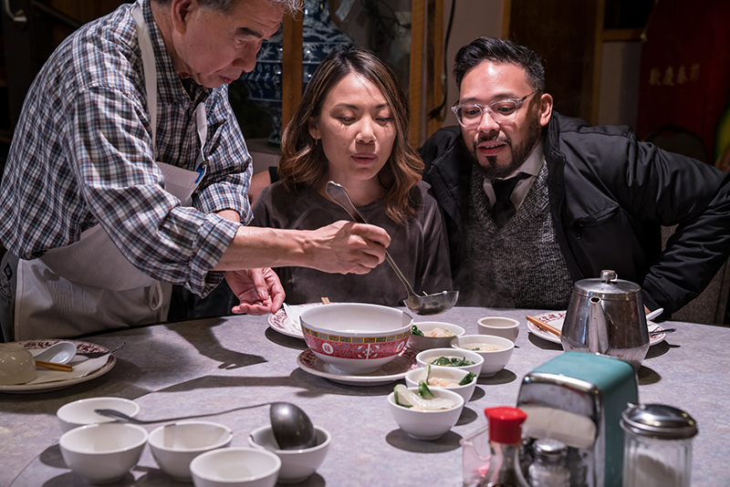 A person ladles steaming soup at a table while tour participants watch during a Wing Luke Food Tour.