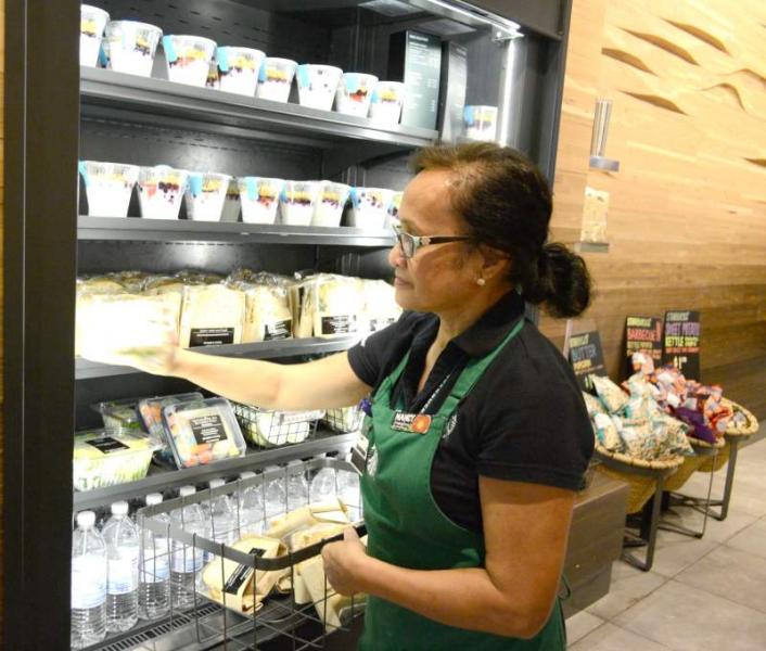 Employee wearing an apron restocking packaged food items in a refrigerated display.