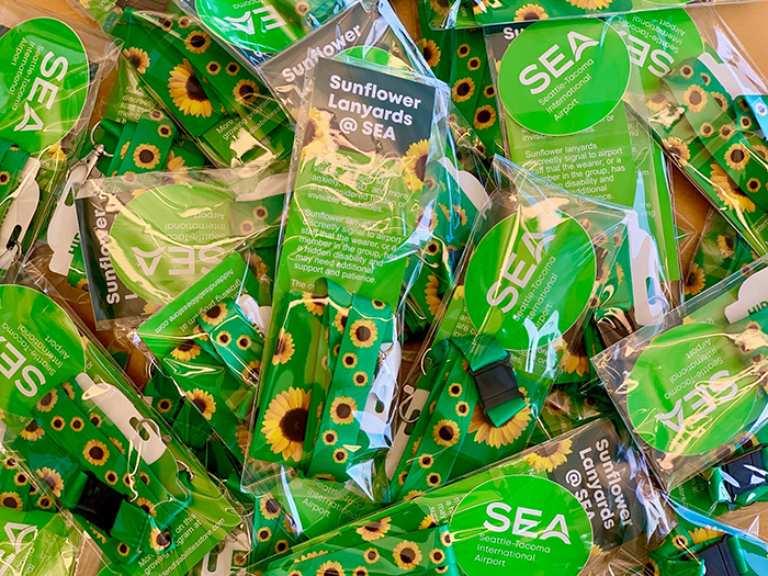 A pile of packaged sunflower-pattern lanyards with green SEA airport information cards visible through the plastic.