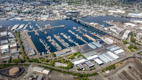 Aerial view of a large waterfront industrial and marina area with multiple docks, boats, warehouses, and surrounding city neighborhoods.