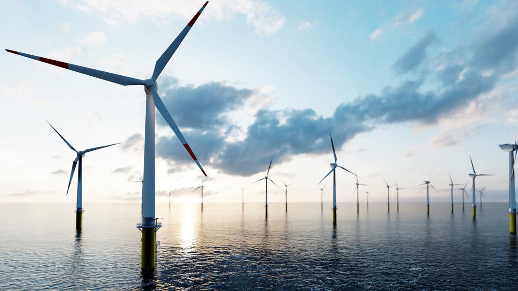 Offshore wind turbines amidst a pink-blue sky with whispy clouds and calm, reflective water.