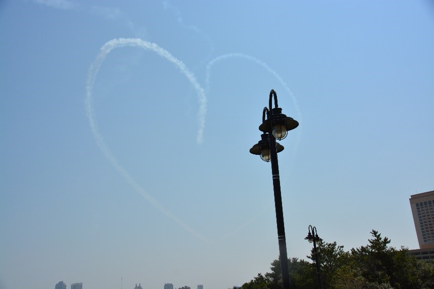 Skywriting forming a heart shape in the sky above a tall streetlamp.