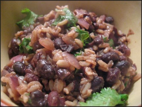 Close-up of a bowl filled with cooked black beans mixed with rice, red onion pieces, and fresh cilantro.