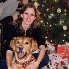 Annbelle Goavec beside a golden retriever, posed in front of a decorated Christmas tree with wrapped presents underneath.