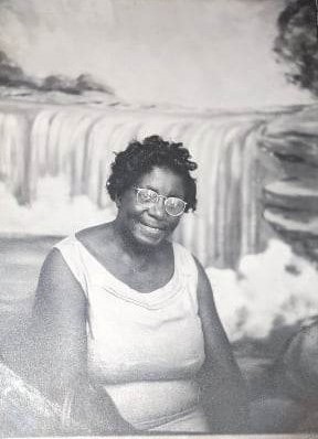 A black‑and‑white portrait of a Great Grandma Addie Mae sitting in front of a painted waterfall backdrop.