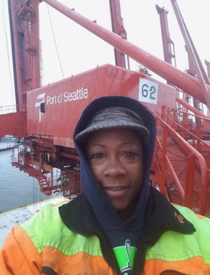 Kelly Simmons wearing safety gear standing in front of large red equipment labeled Port of Seattle.