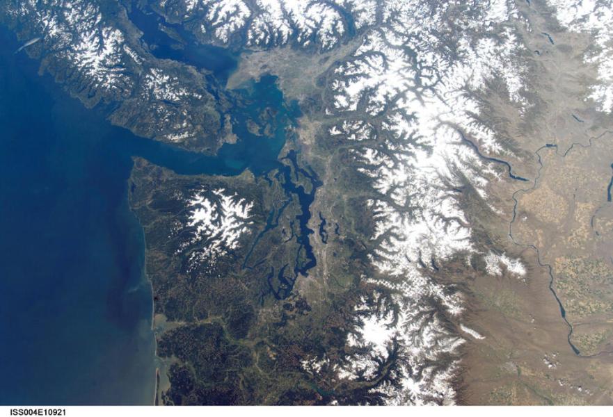 Satellite view of snow‑covered mountains and waterways around western Washington.