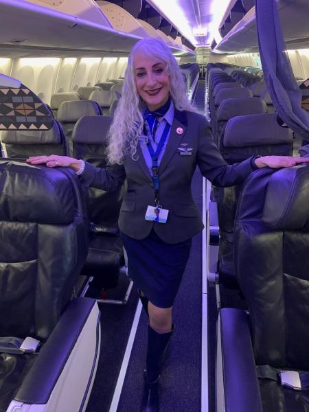 Natalie Razor in an airline uniform stands in the aisle of an airplane cabin, holding the seatbacks on both sides.