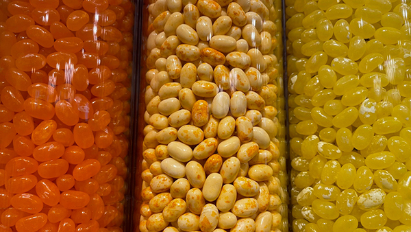 Jars filled with bright orange, speckled light yellow, and solid yellow jelly‑bean candies arranged side by side.