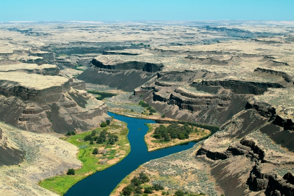 A winding river cuts through a wide, rugged canyon of layered cliffs and dry terrain.