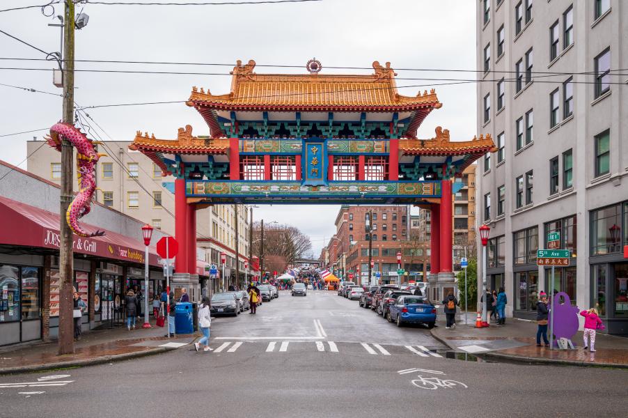 Entrance to the Chinatown–International District shown by a large decorative archway spanning the street, with shops, cars, and pedestrians along the surrounding roadway.