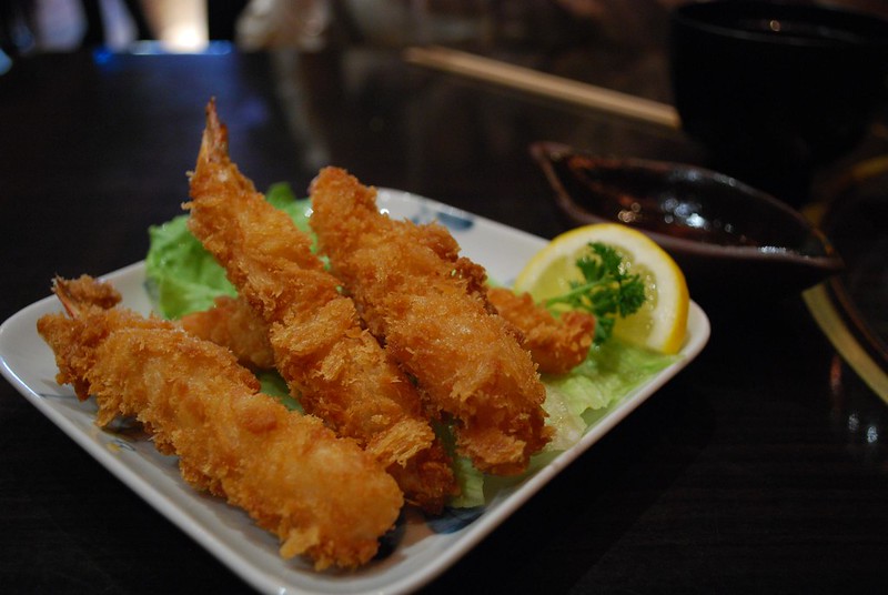 Plate of deep-fried breaded shrimp served on lettuce with a lemon wedge and dipping sauce on the side.