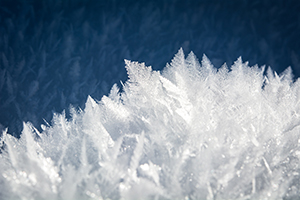 Close-up view of delicate ice crystals forming sharp, feathery patterns on a snowy surface.