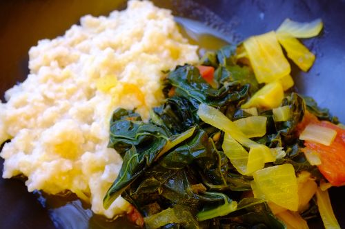 Plate with a serving of creamy mashed potatoes beside cooked leafy greens mixed with diced yellow and red vegetables.