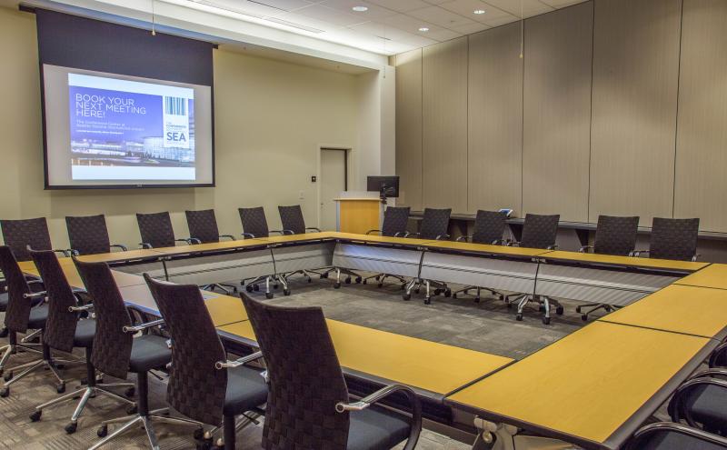 View from inside the Seoul Conference room showcasing a Hollow Square set for 24 people, the podium, and dropdown projector screen