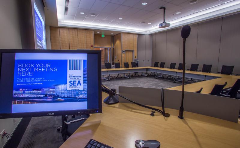 View from the podium located inside the Amsterdam Conference room featuring a hollow square room set with the projector and dropdown screen
