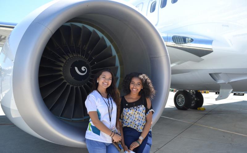 Two interns happily pose by an airplane turbine.
