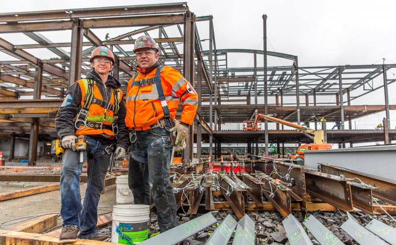 Construction workers standing with tools in front of the beams on a 2 or 3 story building