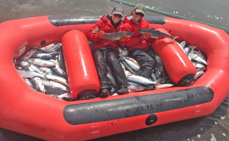 Evelyn Clark next to friend holding salmon in fishing raft.