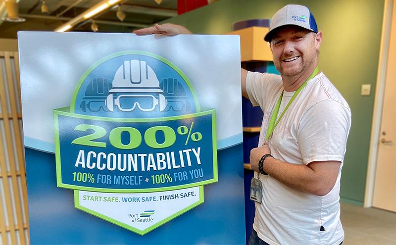 Wireman Foreman Chris Todd stands next to a poster promoting the Port's commitment to 200% accountability