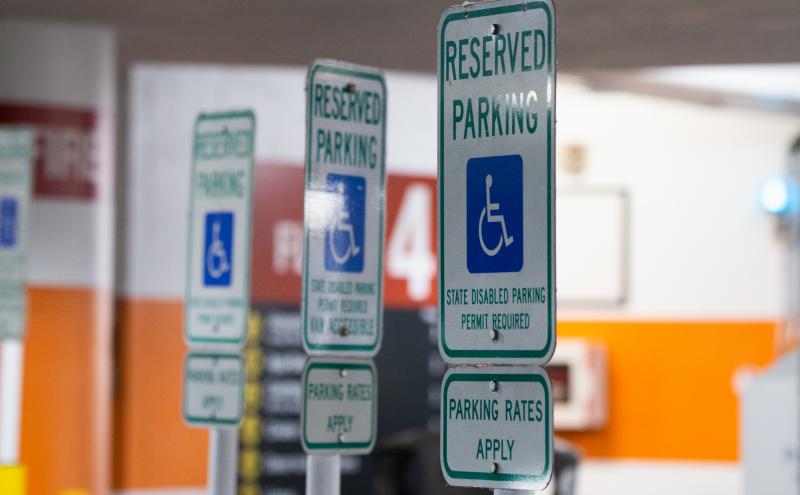 Multiple signs in a parking garage marked ‘Reserved Parking’ with the wheelchair symbol and text stating ‘State disabled parking permit required’ and ‘Parking rates apply.