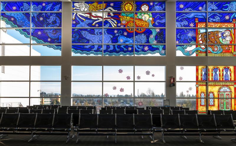 Full stained glass window spanning the upper portion of the airport gate wall, with clear windows and seating below.
