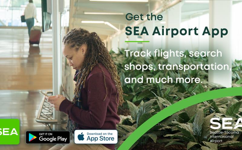 A person with long braided hair stands in an airport terminal holding a smartphone near a seating area. Large green plants line the right side of the space, and another traveler with luggage is visible in the background. Text on the image promotes the SEA Airport App, stating that it can track flights, search shops, find transportation, and more. Logos for SEA, Google Play, and the App Store appear at the bottom.