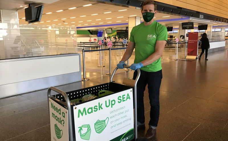 Commissioner Ryan Calkins pushing the mask UP SEA cart wearing a green shirt.