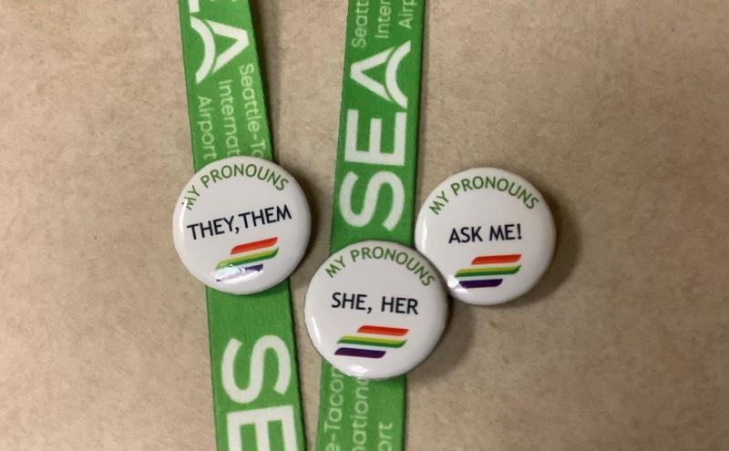 Buttons with personal pronouns on a SEA Airport lanyard.