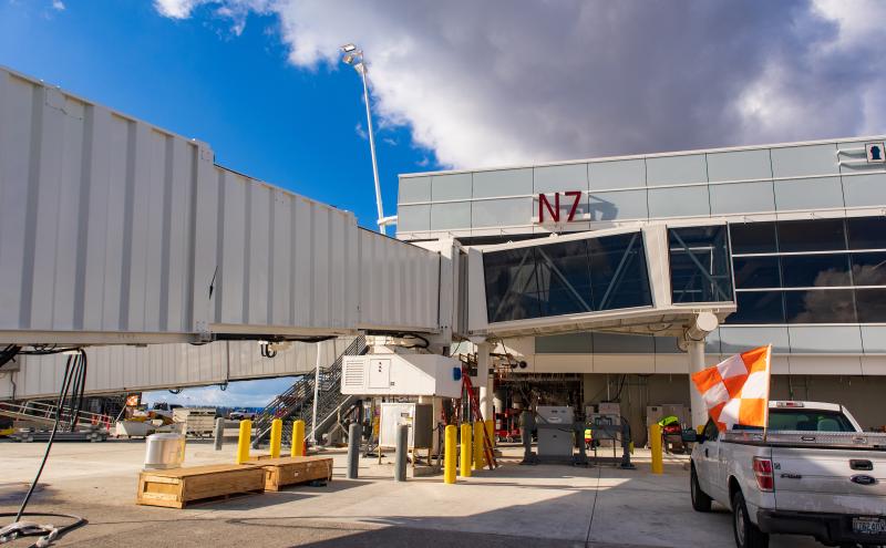 An airport jet bridge at gate N7 with equipment and a pickup truck on the tarmac.