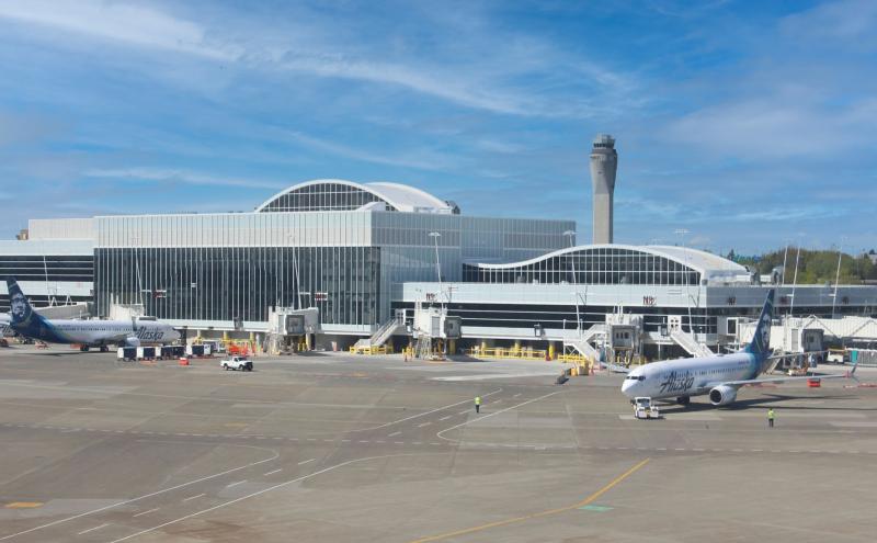 Aircraft parked at multiple gates in front of a modern terminal building, with the airport control tower visible behind them.