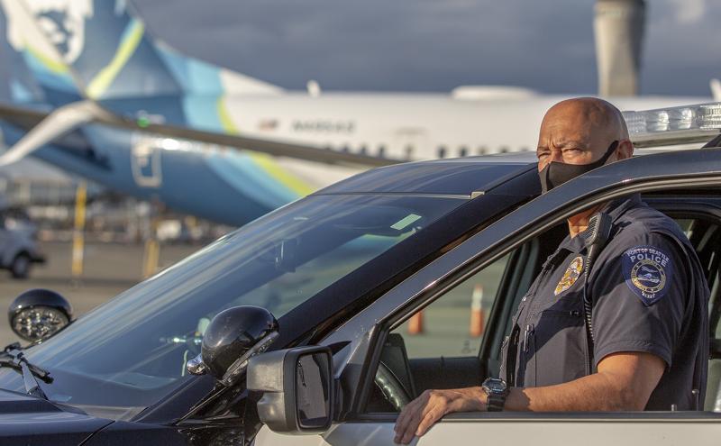 Police officer in uniform standing next to his police cruiser at SEA Airport.