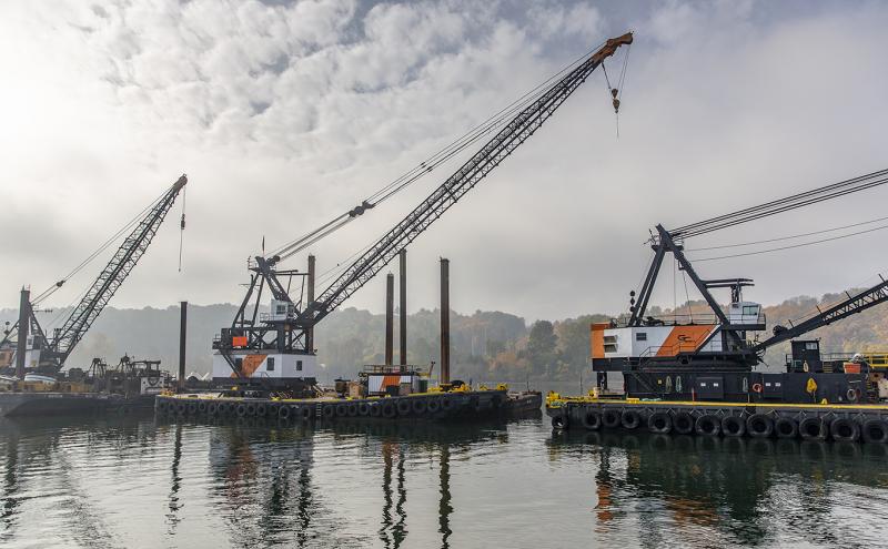 Floating cranes on the Duwamish River in misty air with fall colored bank behind 