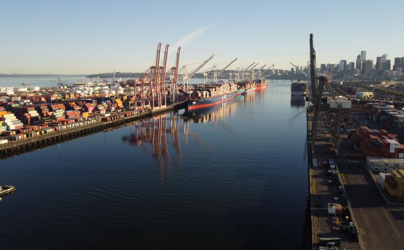 View of the East Waterway looking north. The image shows the channel with a container terminal on each side that has shipping containers, cranes, and container ships docked.